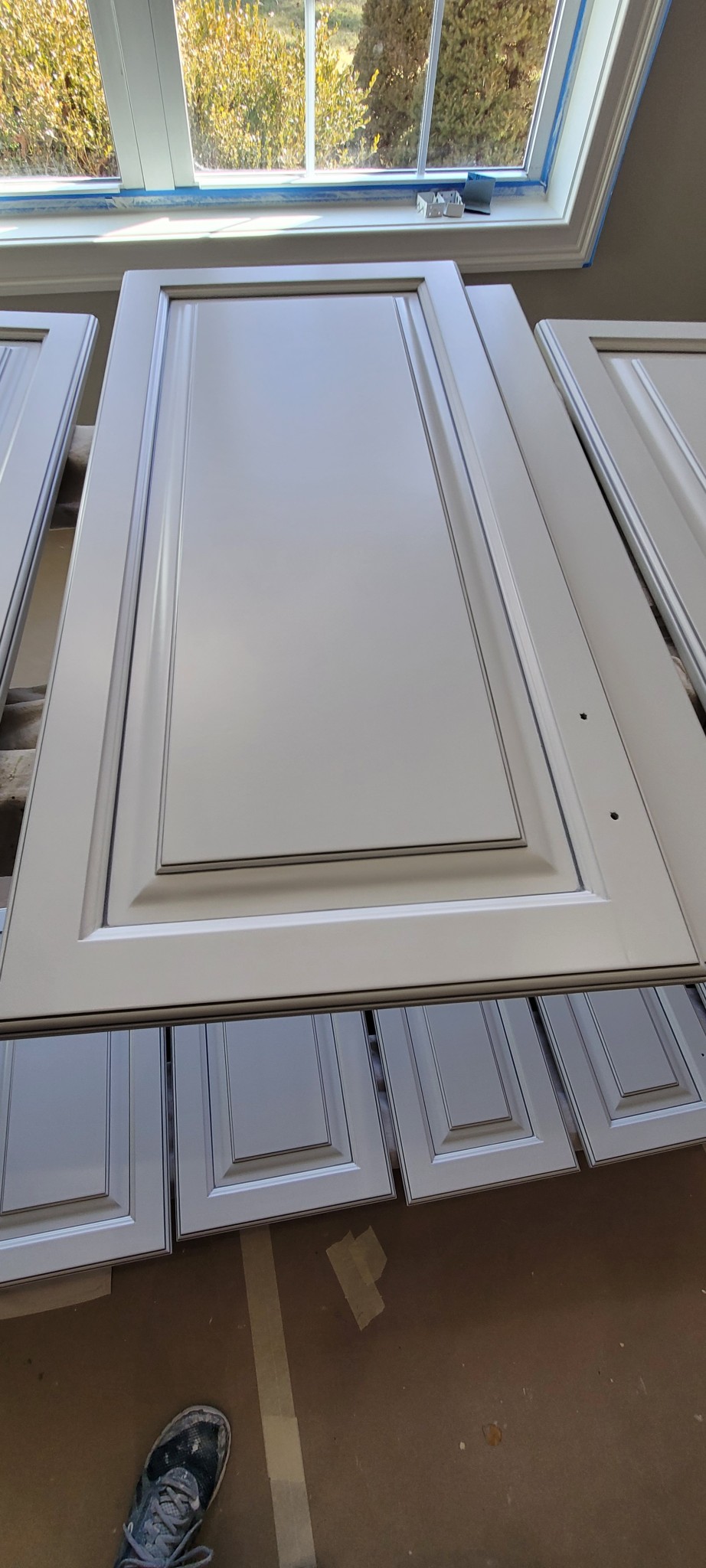 Cabinet doors and drawer fronts painted off-white with gray detailing, drying indoors.