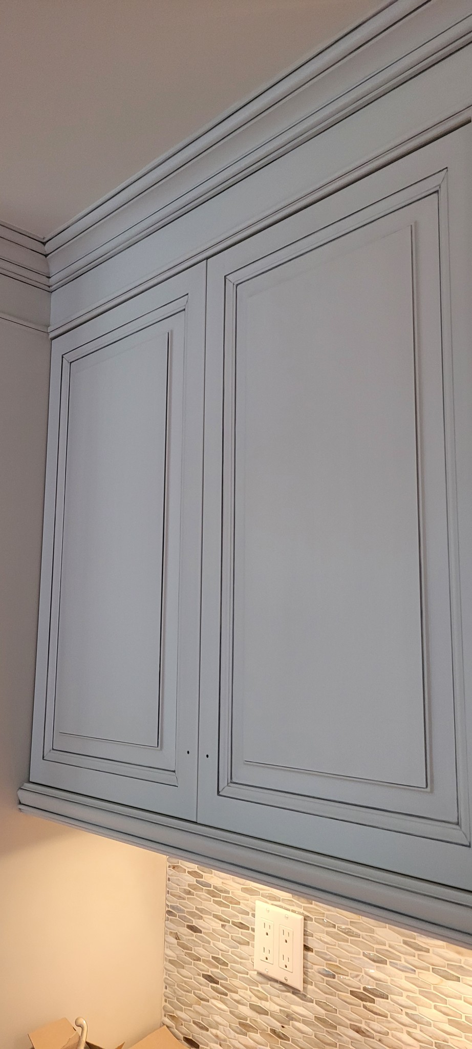 Kitchen upper cabinets with crown molding and antiqued light gray finish.