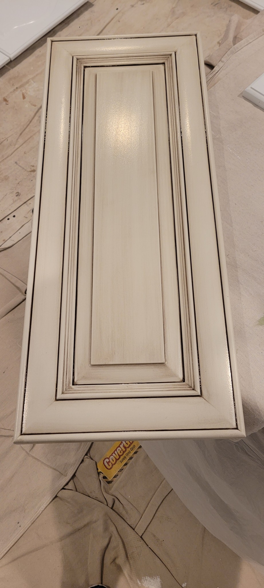 Off-white cabinet door with antiqued glazed finish on a drop cloth.