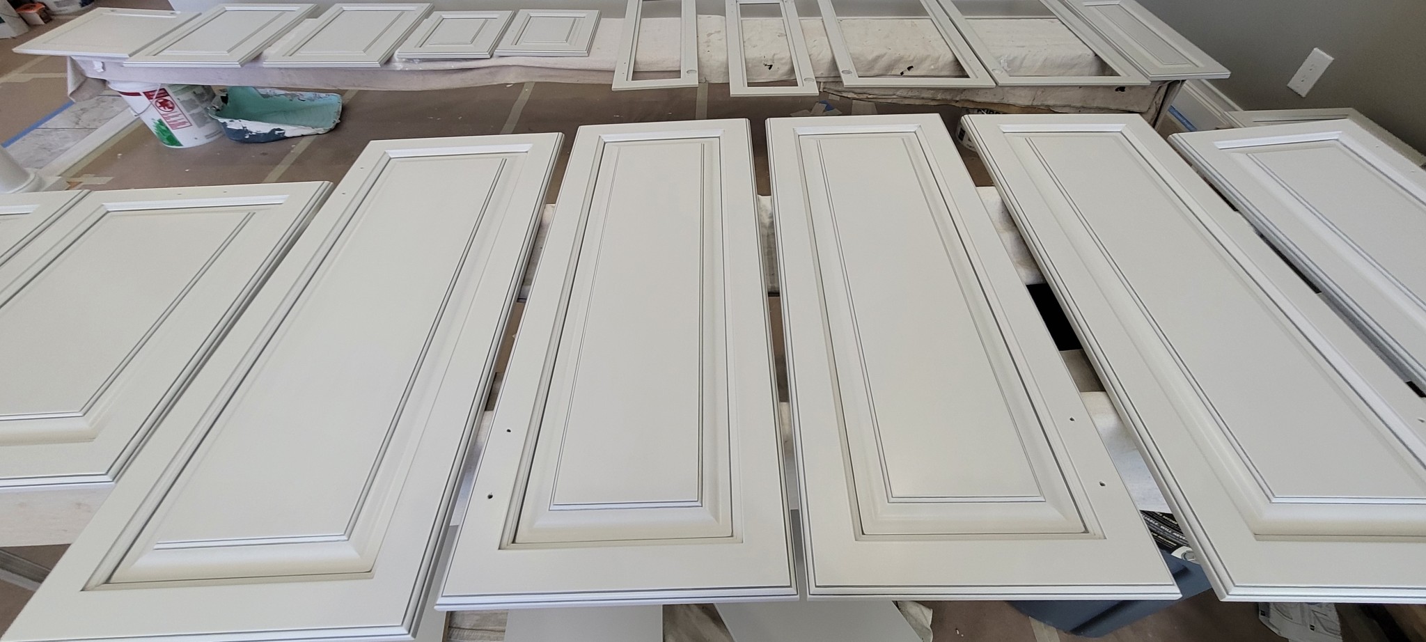 Off-white kitchen cabinet doors and drawer fronts in various stages of refinishing.