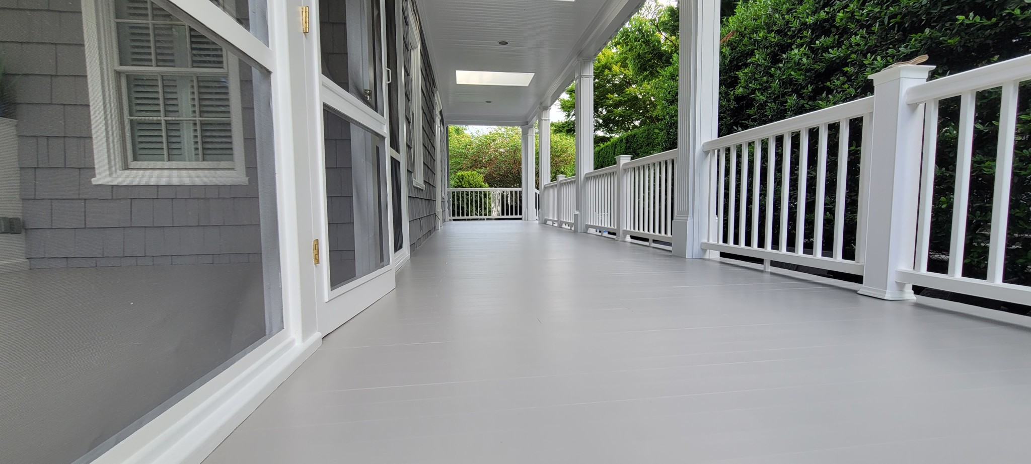 Exterior porch with painted ceiling, columns, railings, and deck in gray and white.