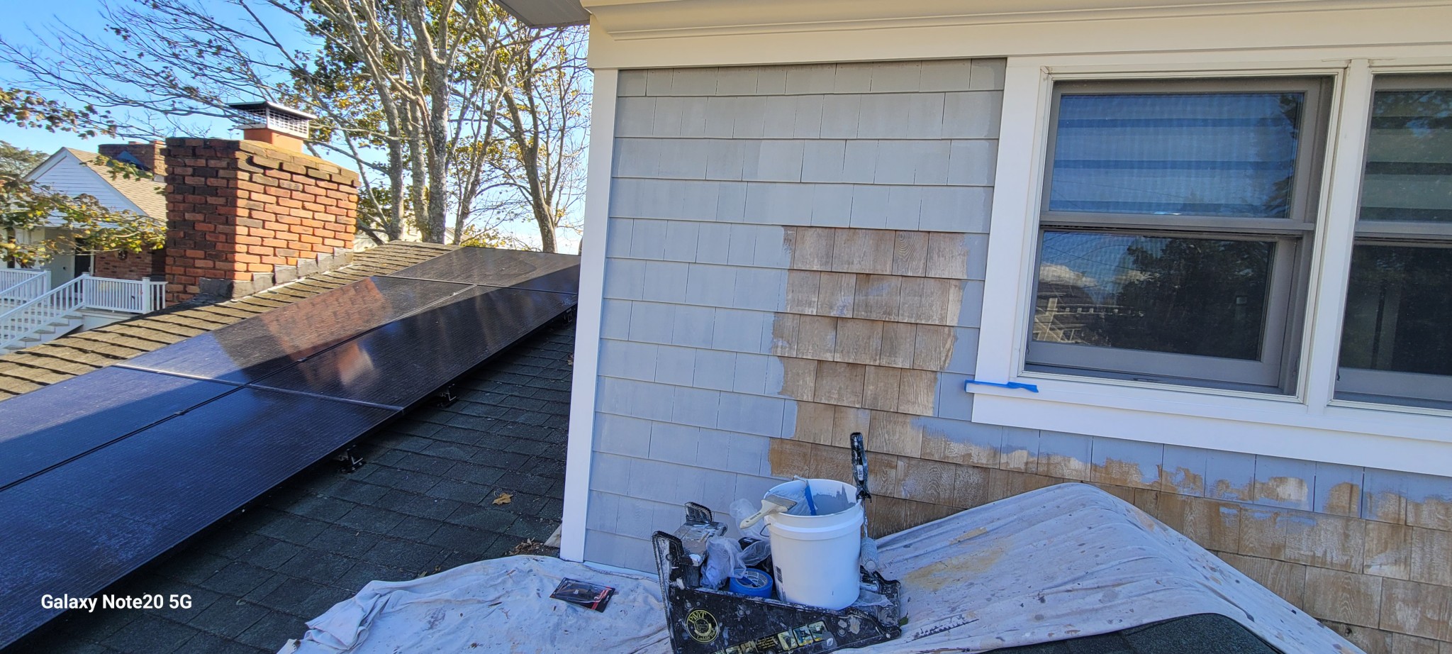 Exterior wood shingles and window trim being prepared and painted light gray.