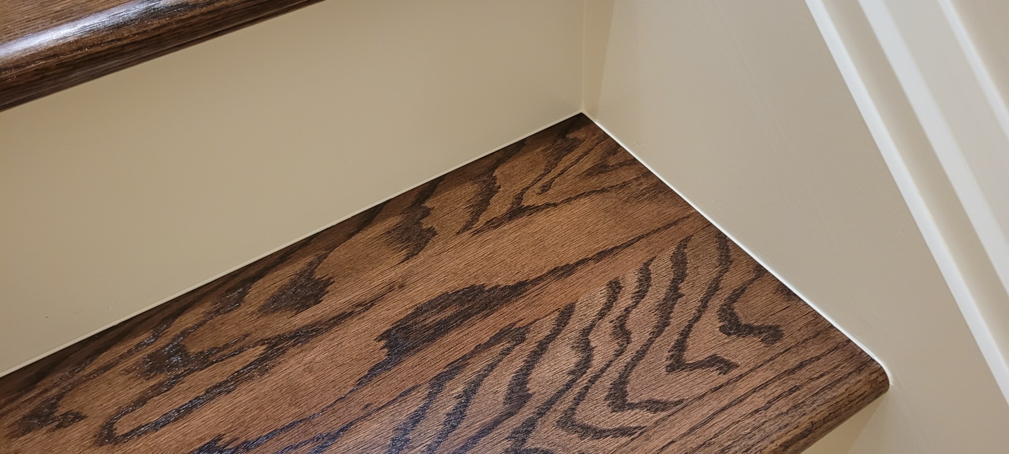 Staircase risers and stringer painted in off-white, contrasting with stained treads and handrail.
