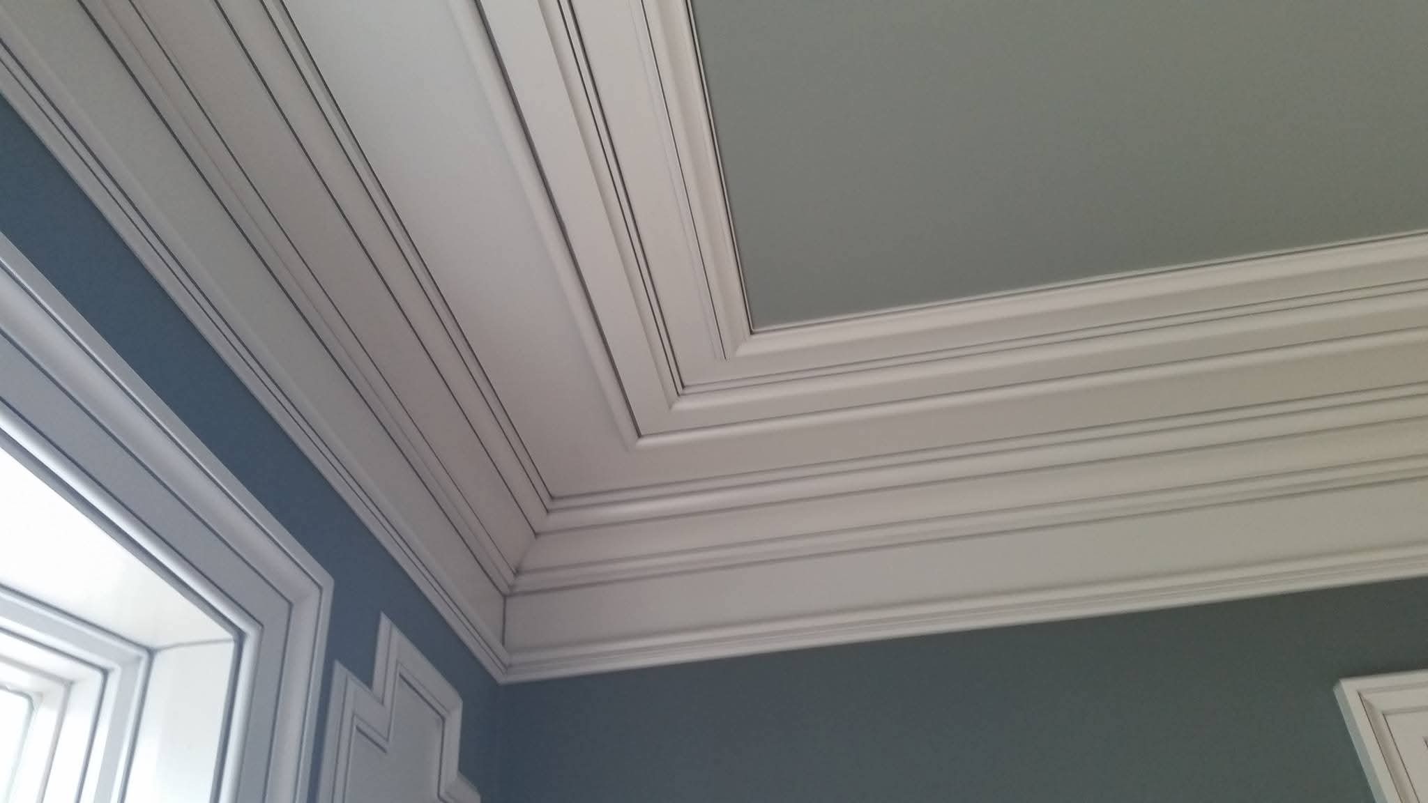White multi-layered crown molding, ceiling, and wall trim in an interior room.