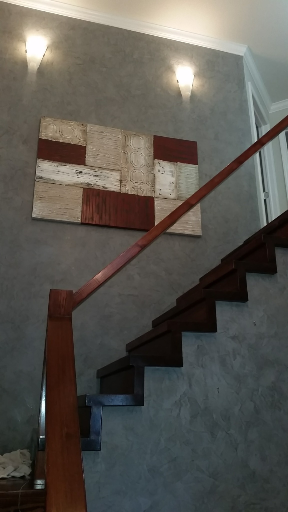 Gray venetian plaster wall with white crown molding and stained wood stair handrail.